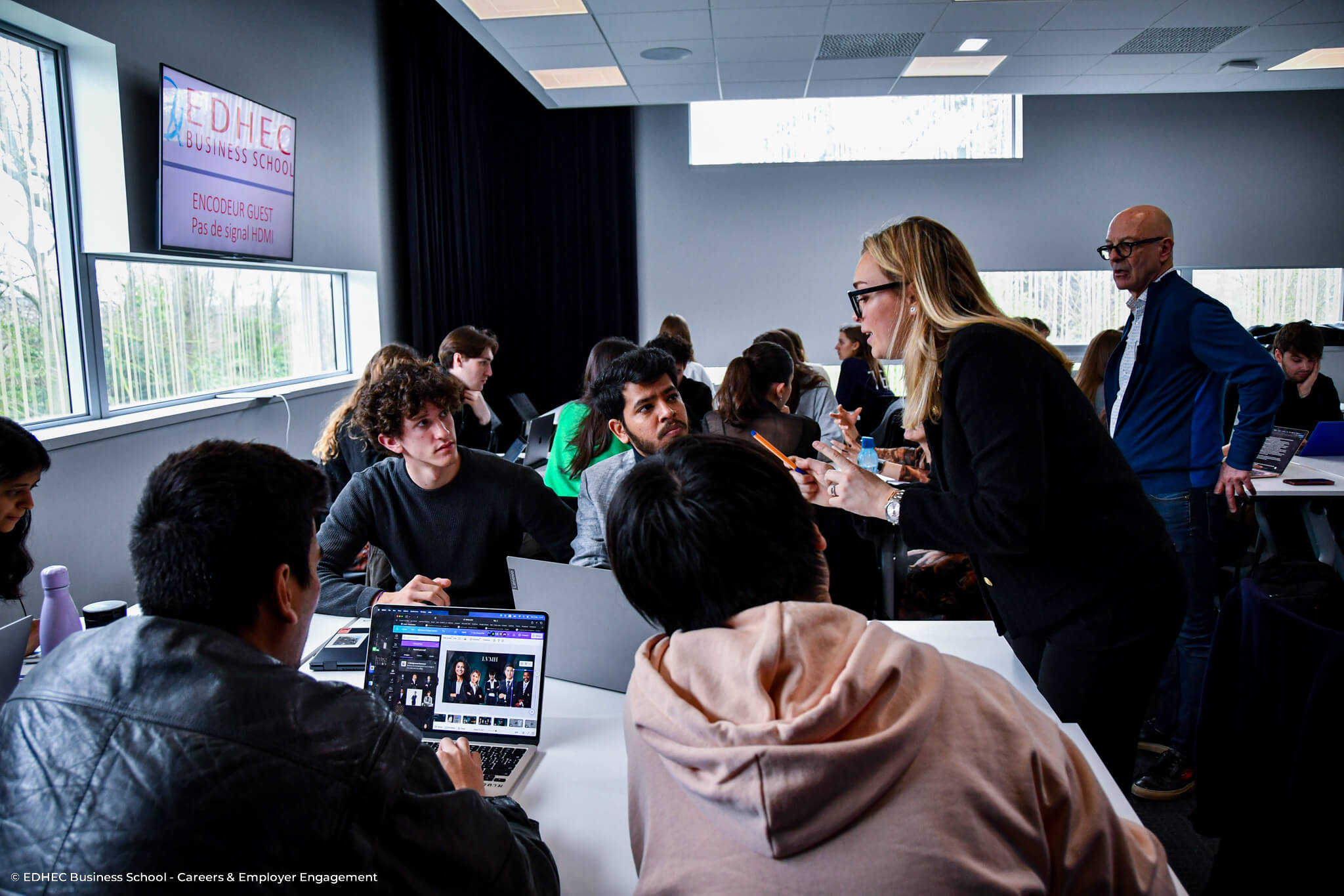 Étudiants assis autour d'une table écoutant une facilitatrice se tenant debout leur donner des conseils