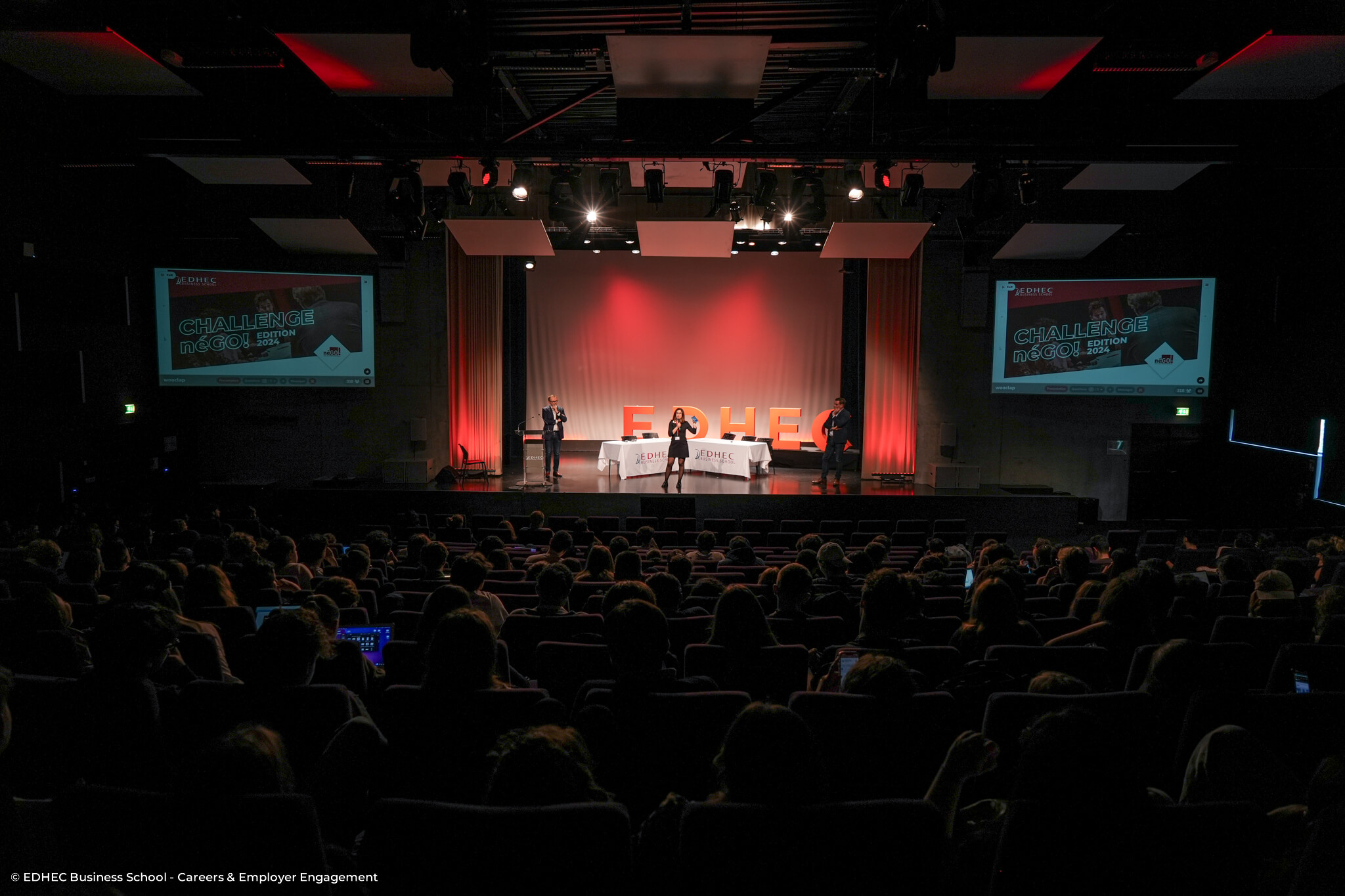Amphithéâtre avec trois intervenants sur scène
